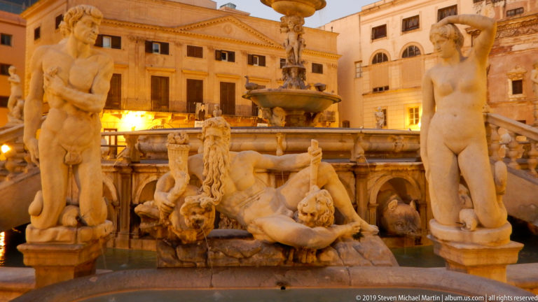 The illuminated tiers and marble figures of Fontana Pretoria stand in Piazza Pretoria at dusk.