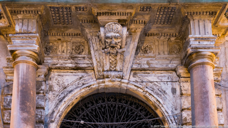 An ornate stone portal with carved panels and a sculpted face surrounds a dark entrance.