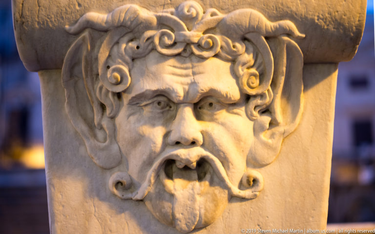 A bearded stone mask with curling hair is carved beneath a projecting fountain basin.