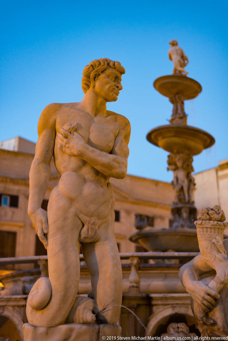 Two marble figures flank the tiers of Fontana Pretoria against the façades of Piazza Pretoria.