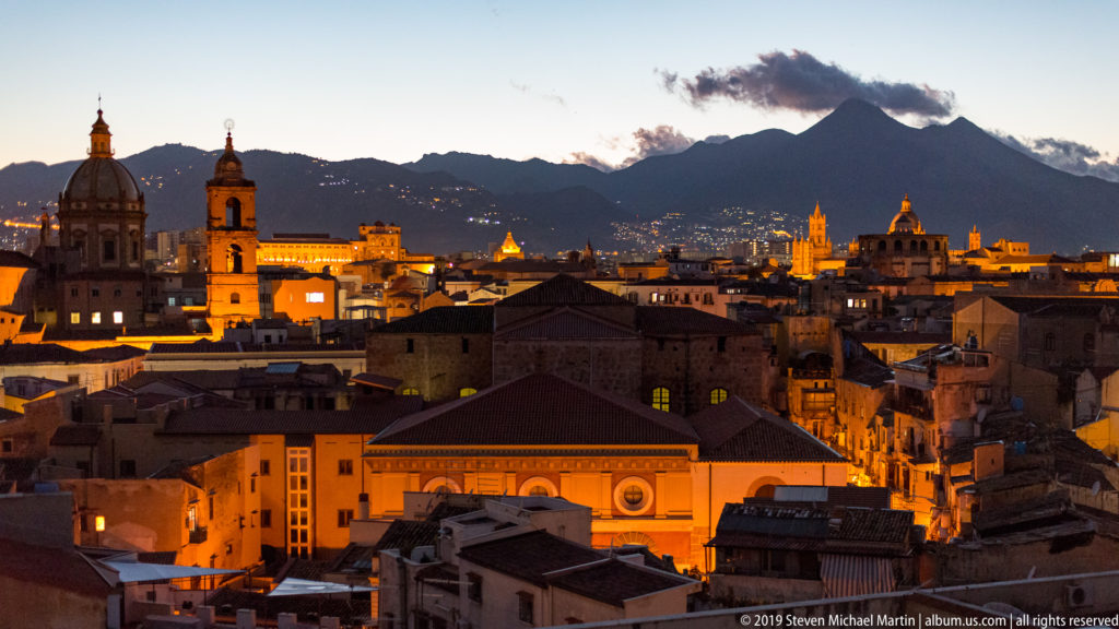 Palermo’s illuminated rooftops and church towers spread beneath Monte Pellegrino after sunset.
