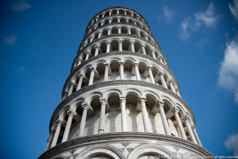 Low-angle view up the Leaning Tower of Pisa, showing stacked round-arched galleries and slender marble columns.