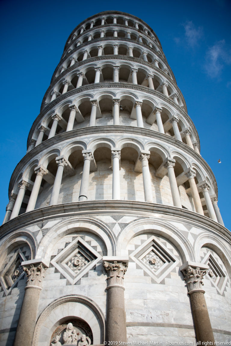 Upward close view of the Leaning Tower’s marble arcades, columns, capitals, and diamond-shaped geometric panels.