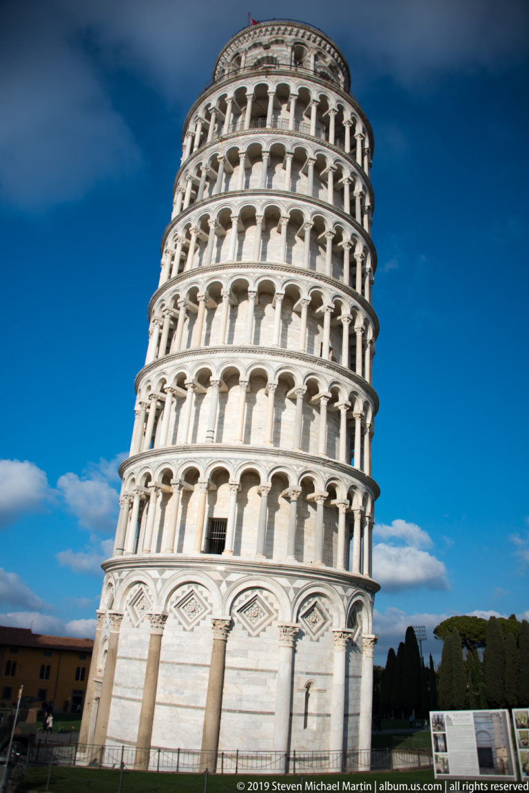 Leaning Tower of Pisa tilting across a blue sky, with stacked marble arcades and a solid decorated base.