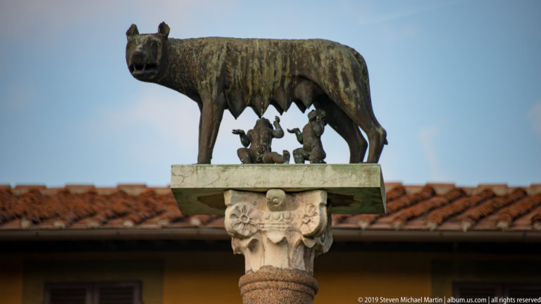 Close view of the Capitoline Wolf nursing Romulus and Remus atop an ornate stone column in Pisa.