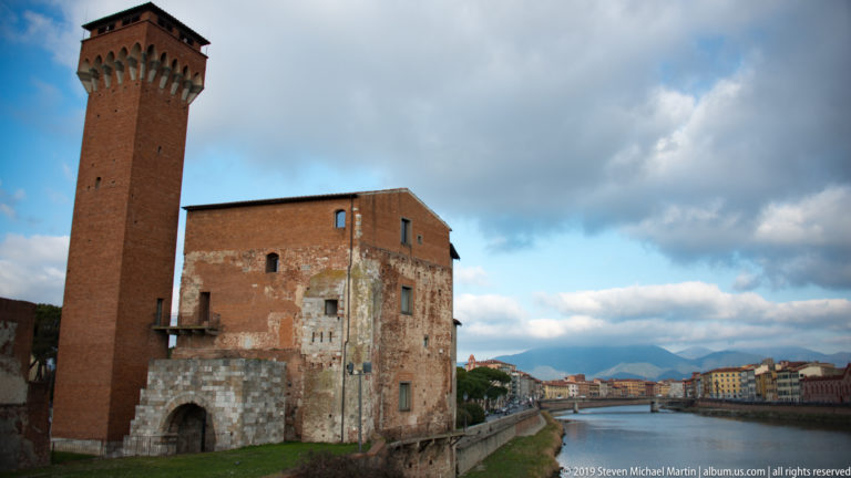 Torre Guelfa rising from the brick-and-stone Cittadella Vecchia beside the Arno River in Pisa.