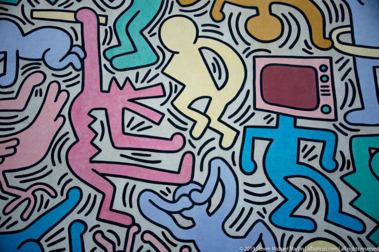 Colorful mural detail with a red television-like screen, pale yellow figure, and interlocking pink and blue forms.