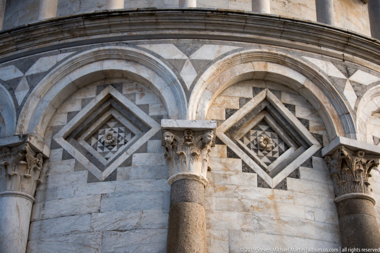 Close architectural detail of the Leaning Tower with blind arches, diamond inlays, columns, and carved capitals.