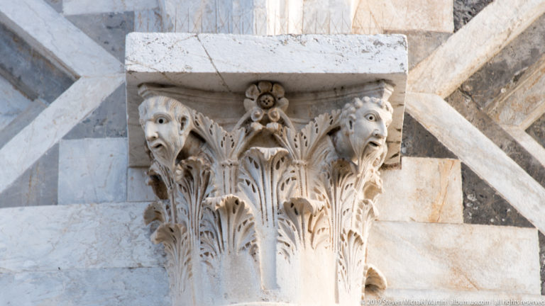 Close view of a marble capital carved with acanthus leaves and two projecting animal heads on the Leaning Tower.