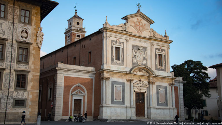 Santo Stefano dei Cavalieri church façade with pale stone ornament, brick side wall, and bell tower in Pisa.