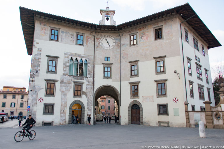 Palazzo dell’Orologio on Piazza dei Cavalieri, showing its clock, central archway, painted façade, and rooftop bell.