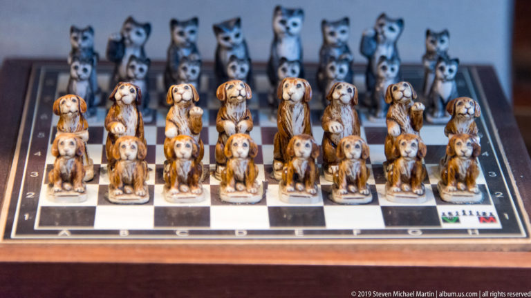 Souvenir chessboard arranged with painted dog figurines in front and cat figurines behind.