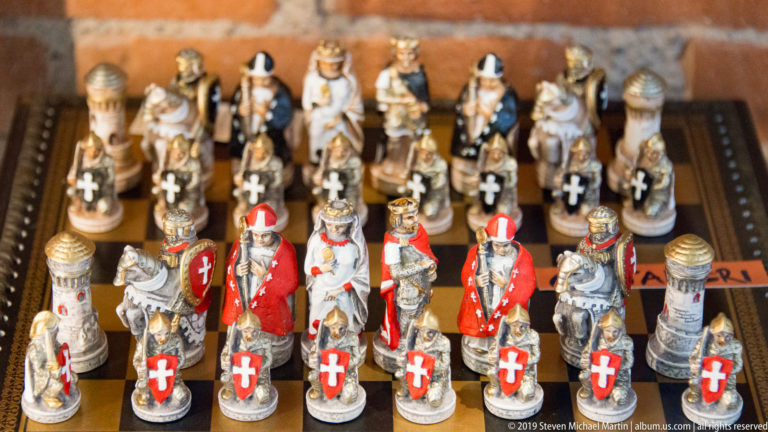 Painted medieval-themed souvenir chess pieces, including armored and clerical figures, arranged in rows on a board.