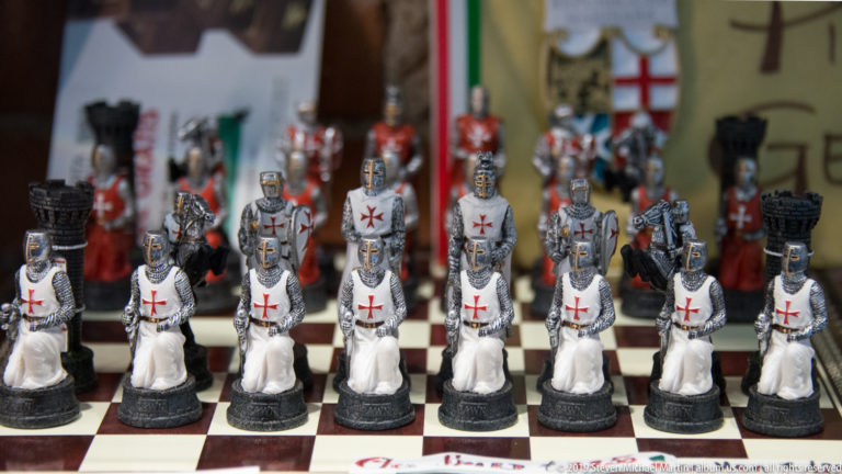 Rows of medieval-style chess pieces with red crosses on white tunics and shields arranged on a chessboard.