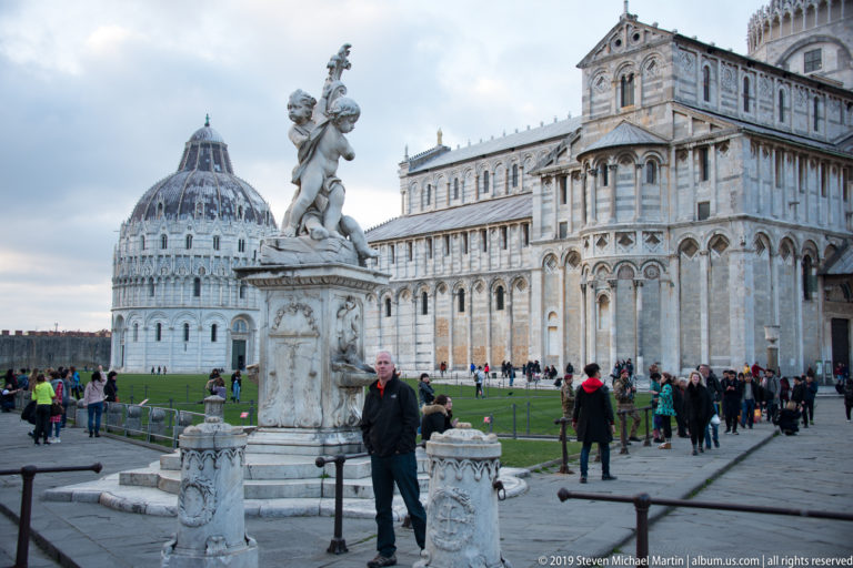Visitor beside the Fontana dei Putti, with Pisa Baptistery and Cathedral extending across the Piazza del Duomo.
