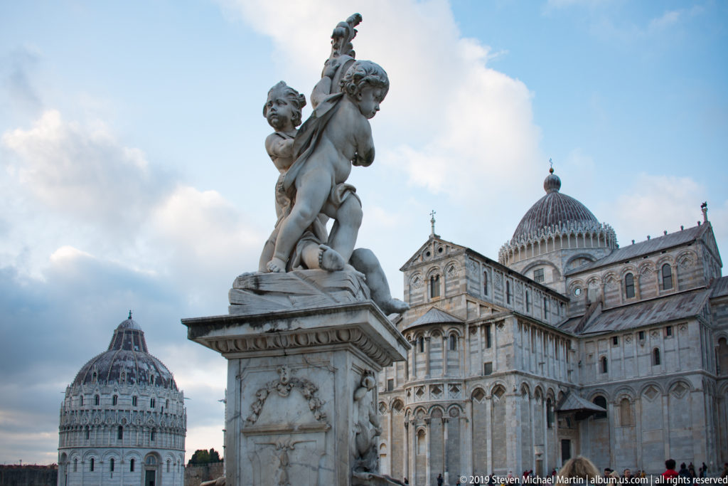 Fontana dei Putti in the foreground with its marble figures, Pisa Cathedral, and the Baptistery rising behind.