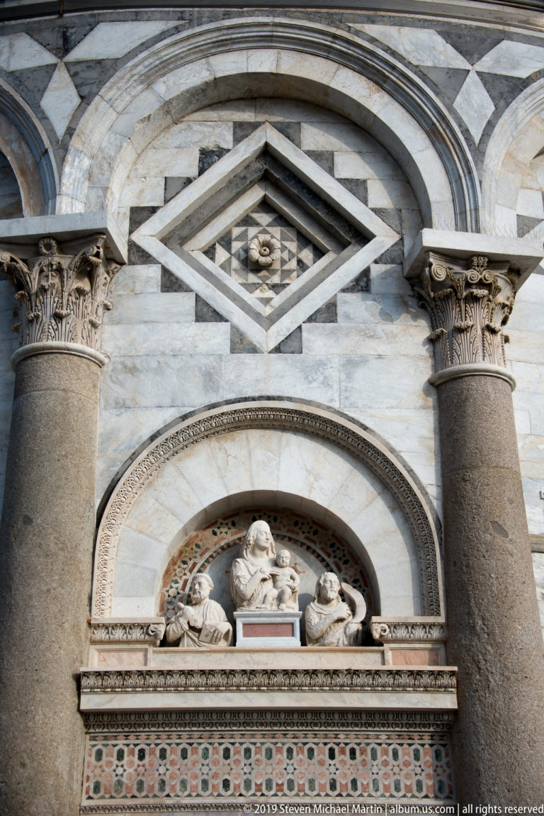 Marian sculptural group in an arched recess beneath geometric marble ornament on the Leaning Tower of Pisa.