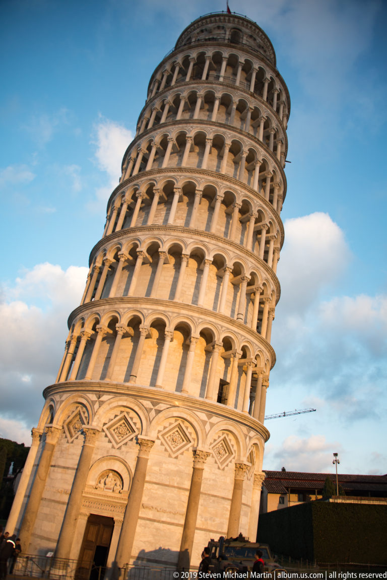 Low-angle oblique view of the Leaning Tower of Pisa, showing its tilted marble base and stacked arcades.