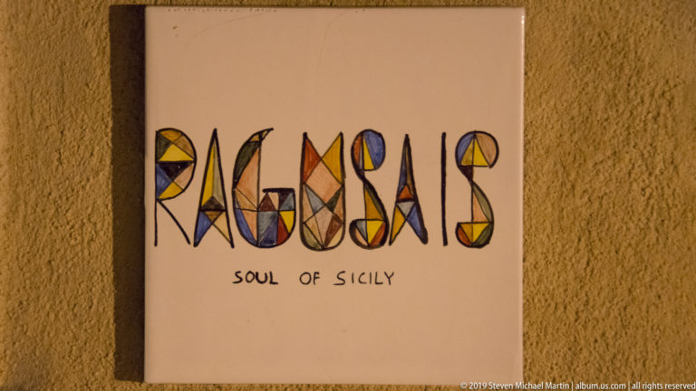 Wall-mounted sign reading “RAGUSA” in colorful geometric lettering with “SOUL OF SICILY” written underneath.