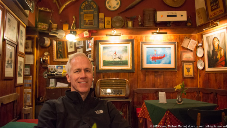 Seated diner in a wood-paneled restaurant filled with framed pictures, plaques, vintage objects, and an old radio.