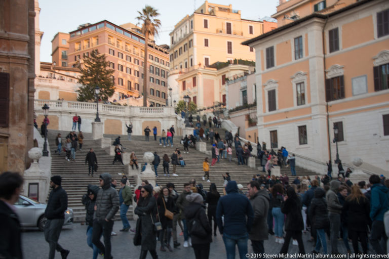 Crowds fill Piazza di Spagna below the broad lower flights of the Spanish Steps and surrounding historic buildings.