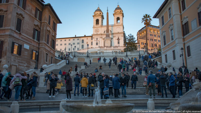 Frontal view up crowded Spanish Steps toward the obelisk and twin towers of Trinità dei Monti.