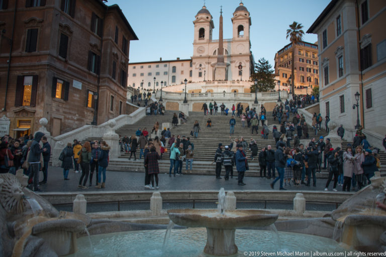 Spanish Steps crowded with visitors, Barcaccia Fountain in foreground, and Trinità dei Monti above.