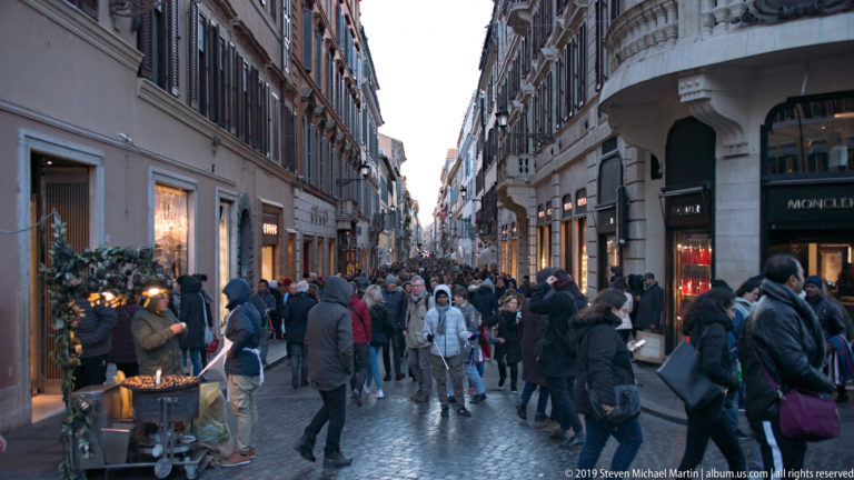 Crowded cobbled Via dei Condotti lined with shops and historic façades near Piazza di Spagna in Rome.