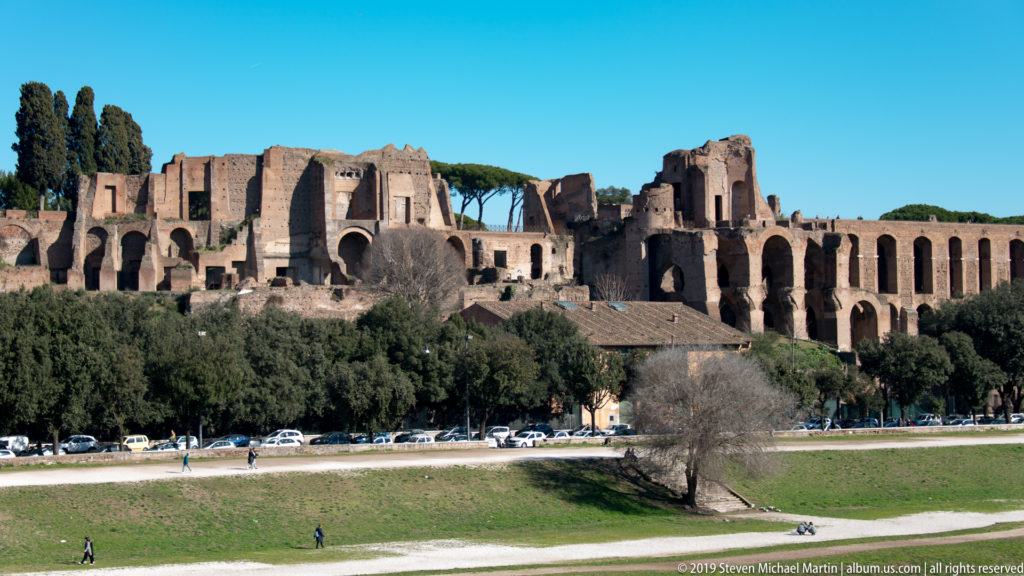 Palatine Hill palace ruins with brick arches and umbrella pines above the open Circus Maximus field.