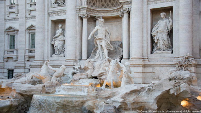 Oblique view across Trevi Fountain with Oceanus, flanking statues, sea horses, rockwork, and illuminated water.