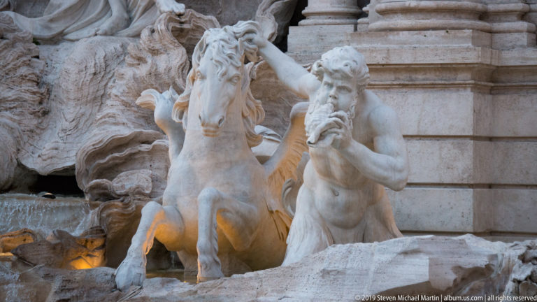 Close view of a stone sea horse and muscular attendant emerging from rockwork at the Trevi Fountain.