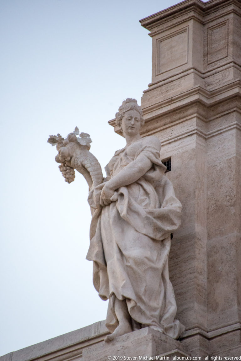 Low-angle view of a robed female allegorical statue with an extended arm on the Trevi Fountain façade.