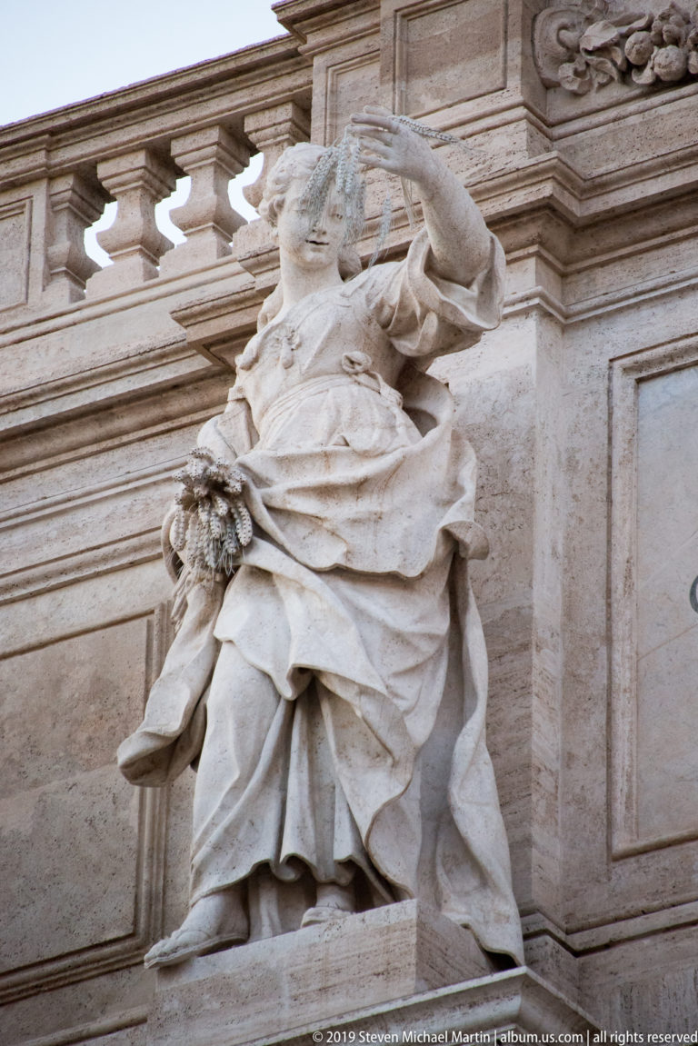 Seated robed female allegorical statue holding an attribute in a niche on the Trevi Fountain façade.
