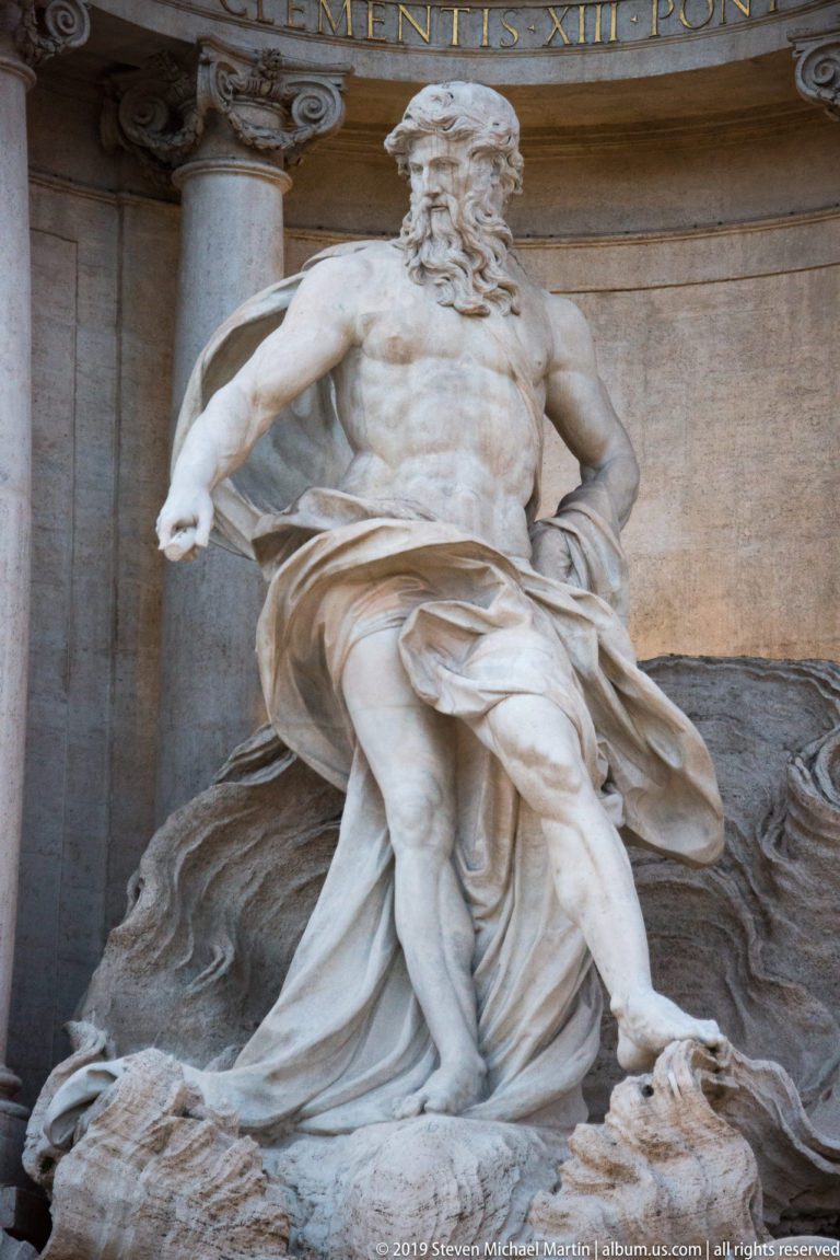 Close view of the bearded Oceanus statue with muscular torso and flowing drapery at the Trevi Fountain.