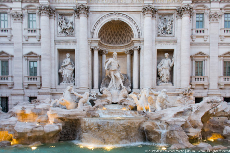 Frontal view of Trevi Fountain with central niche, flanking statues, sea horses, rockwork, and illuminated basin.