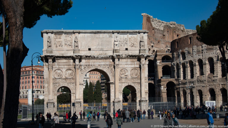Arch of Constantine in front of the Colosseum with crowds gathered around the archaeological area.