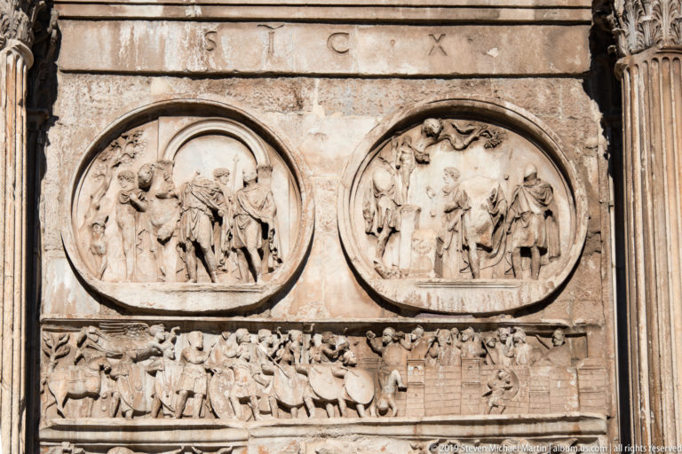 Two circular Roman reliefs above a crowded rectangular frieze on the Arch of Constantine.