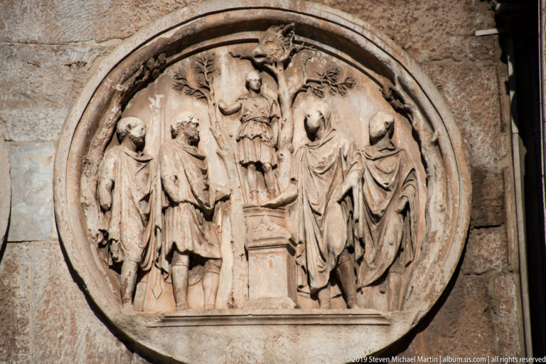 Circular Roman relief with several standing figures arranged around a central raised figure on the Arch of Constantine.