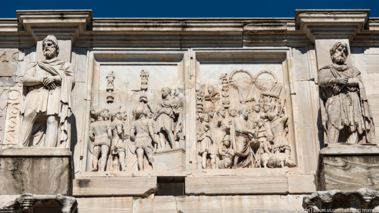 Upper Arch of Constantine with narrative relief panels and standing captive figures above Corinthian columns.