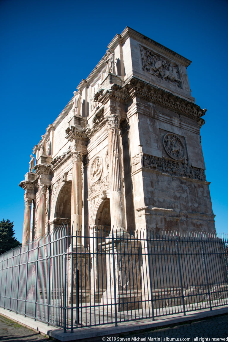 Low-angle oblique view of the Arch of Constantine with columns, relief panels, roundels, and inscribed attic.