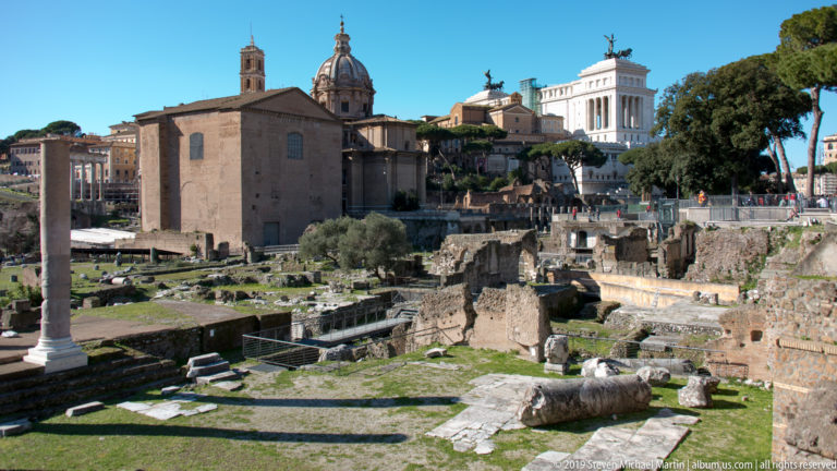 Forum ruins with columns and foundations below Santi Luca e Martina and the distant white Vittoriano.