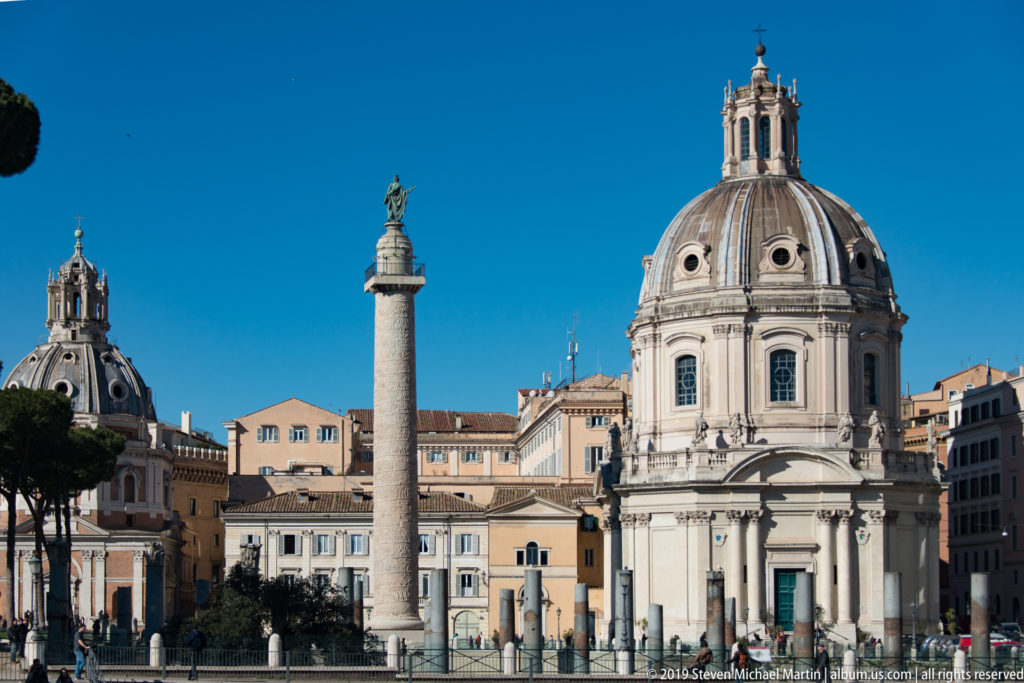 Trajan's Column and domed churches rising behind ancient columns and excavated remains at Trajan's Forum.