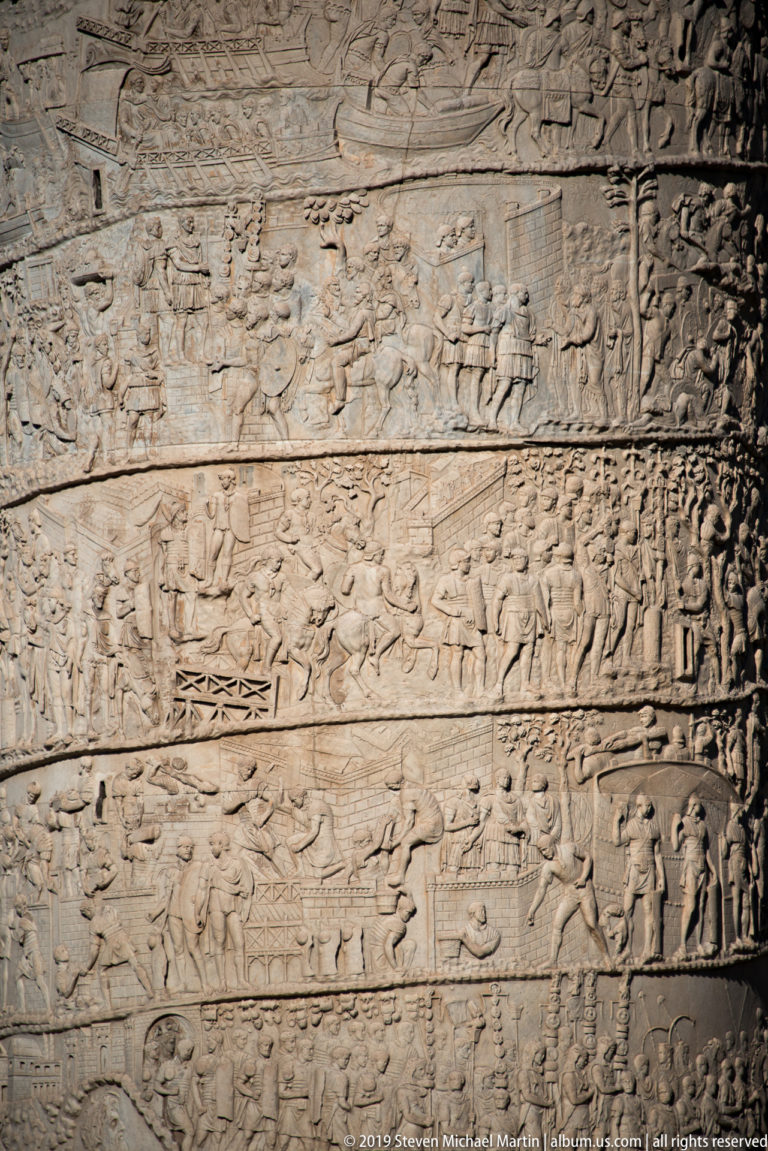 Detailed spiral bands on Trajan's Column showing soldiers, buildings, camps, boats, and grouped figures.