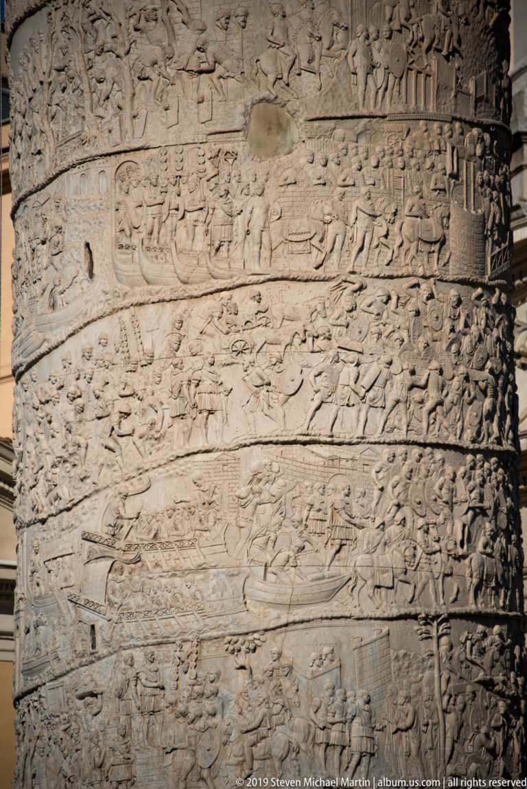 Close view of Trajan's Column relief with soldiers, boats, fortifications, buildings, and marching figures.