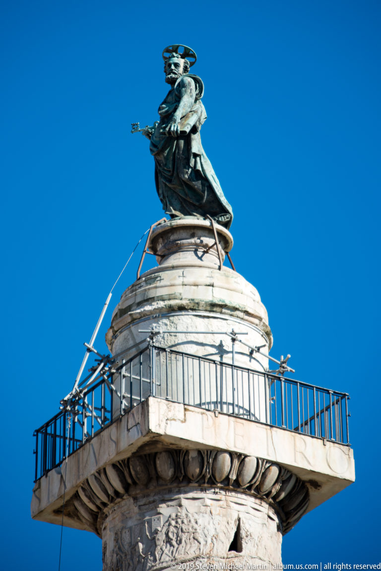 Saint Peter statue above the carved capital, viewing platform, and spiral reliefs of Trajan's Column.