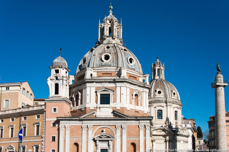 Domed Santa Maria di Loreto beside the upper portion of Trajan's Column under a clear blue sky.