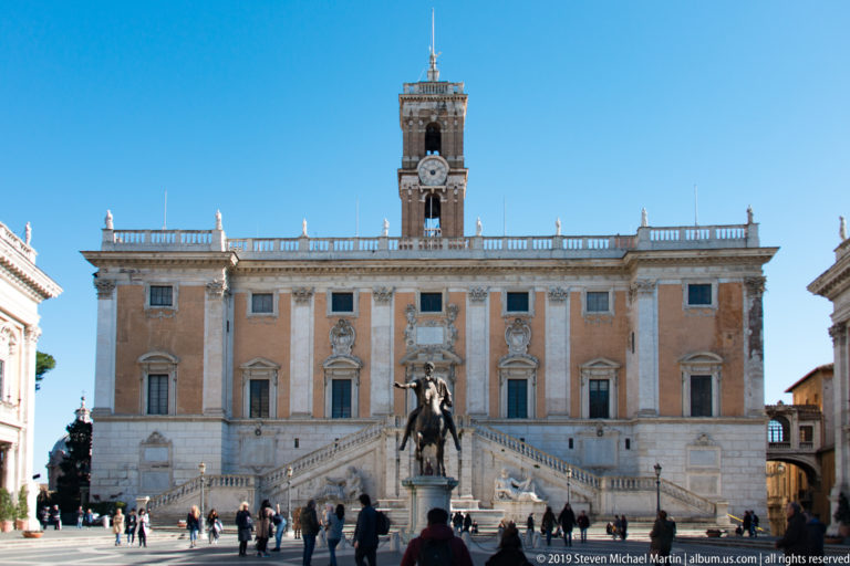 Palazzo Senatorio with broad double staircase, central clock tower, and equestrian statue in Piazza del Campidoglio.