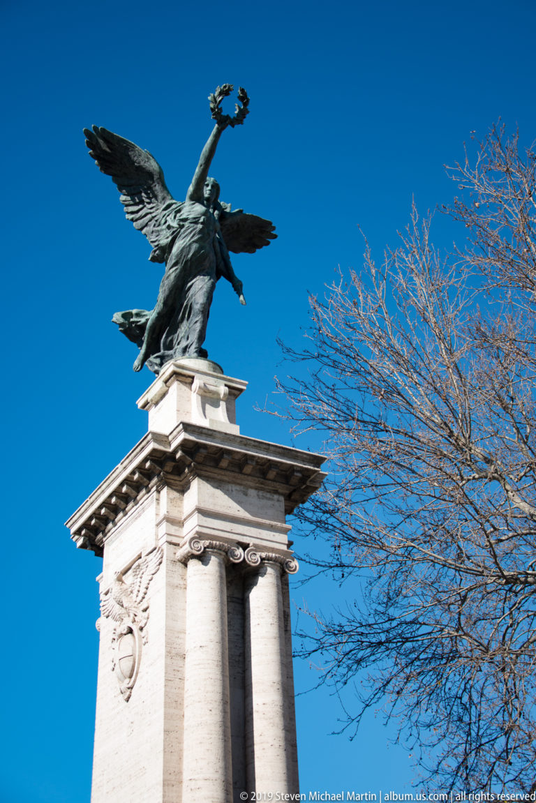 Marble angel holding a Passion symbol on a high pedestal along Ponte Sant’Angelo in Rome.