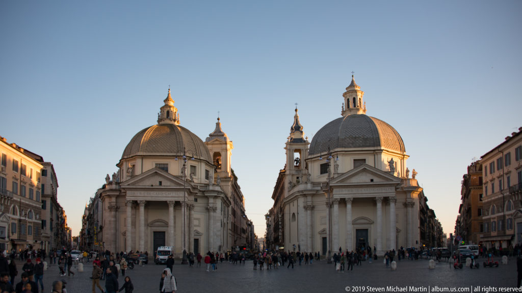 Twin domed churches with columned porticoes facing Piazza del Popolo, with pedestrians crossing the open square.