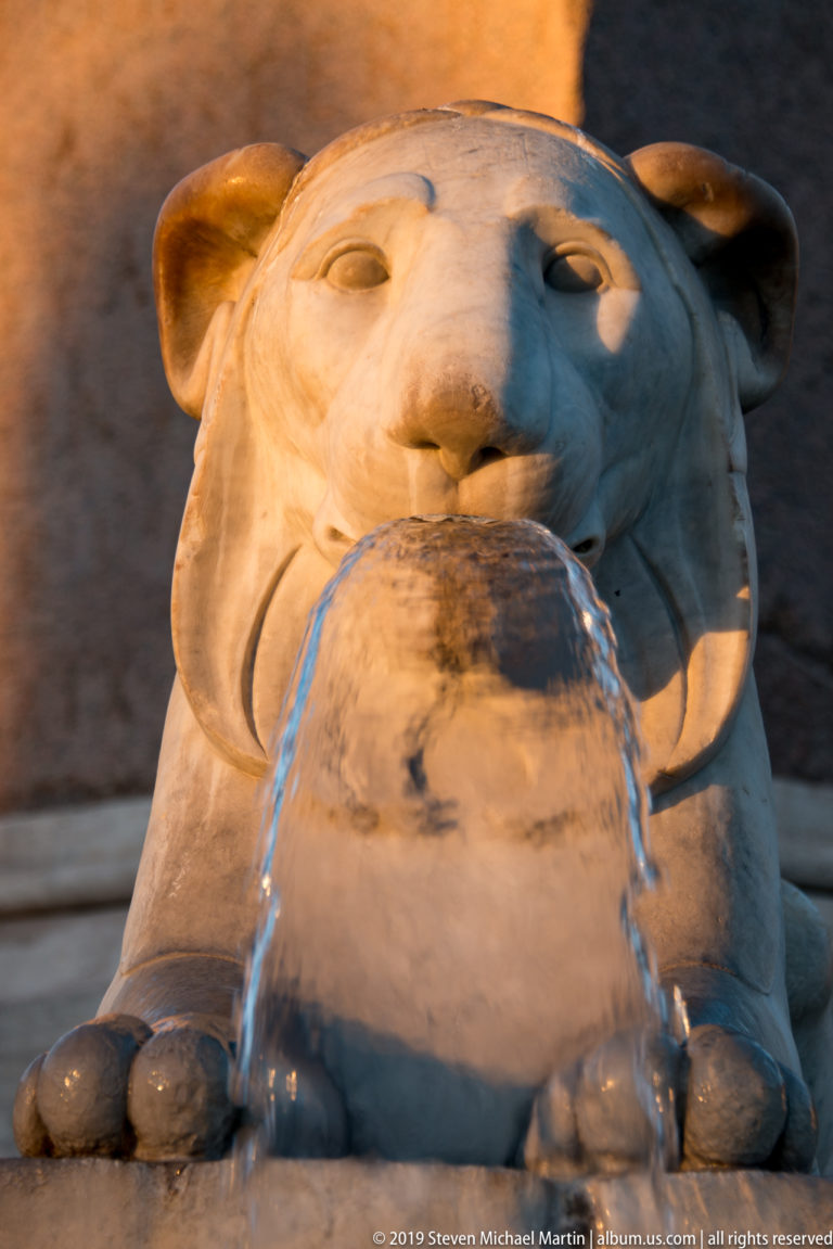 White marble Egyptian-style lion fountain pouring water into a round basin beside the Flaminio Obelisk.